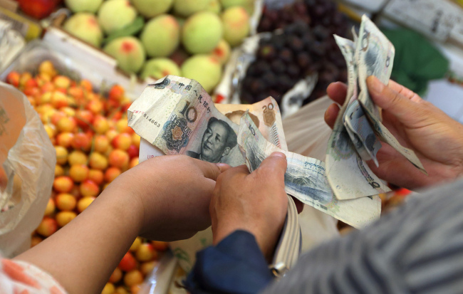A shopper counts Chinese yuan banknotes as he shops for fruit and vegetables at a market in Shanghai.    Bloomberg