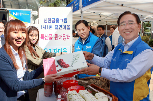 Shinhan Financial Group chairman Han Dong-woo (right) and Shinhan Bank CEO Suh Jin-won (second from right) pose during a social contribution event in which the group provided farmers with a chance to market agricultural products at its headquarters in downtown Seoul on Wednesday.   Shinhan Financial