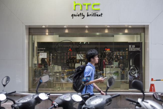 A man uses a mobile device as he walks past an HTC Corp. retail store in Taipei.    Bloomberg