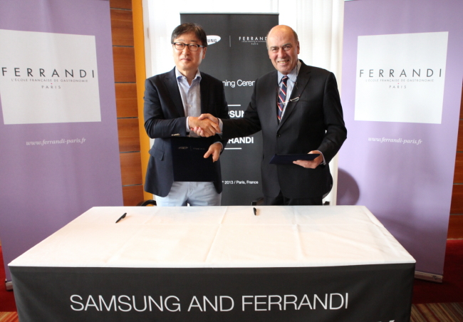 Samsung Electronics’ chief of consumer electronics business Yoon Boo-keun (left) poses with Ferrandi president George Nectoux after signing a pact in Paris over the weekend, under which the Korean conglomerate’s home appliances unit will open cooking classes at the French culinary school.   Samsung Electronics