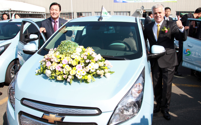 Changwon City Mayor Park Wan-su (left) and GM Korea CEO Sergio Rocha pose with the first Chevrolet Spark EV car produced at the carmaker’s Changwon plant in South Gyeongsang Province on Monday.   GM Korea