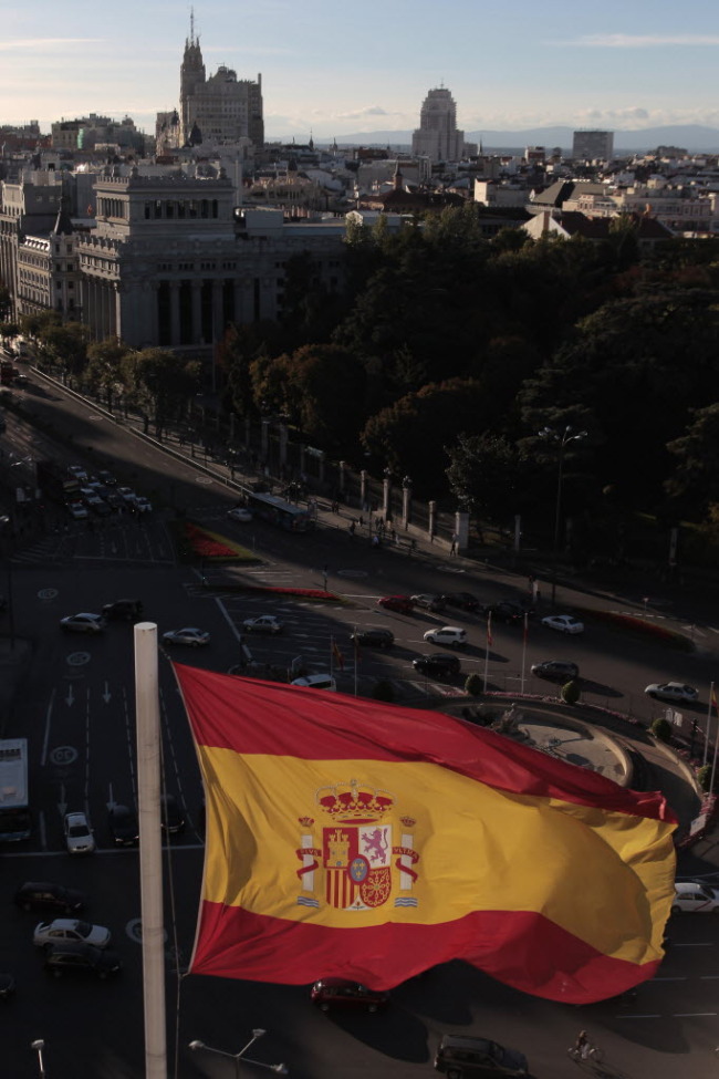 A Spanish national flag flies above the town hall as automobiles maneuver around Cibeles Square in Madrid.  Bloomberg
