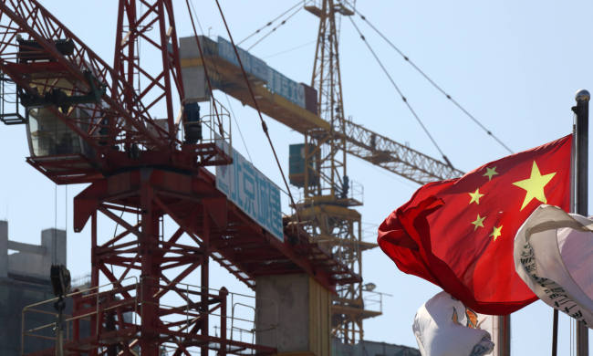 A Chinese flag flies in front of cranes at a construction site in the Fun City apartment complex in the Fangshan district of Beijing.    Bloomberg