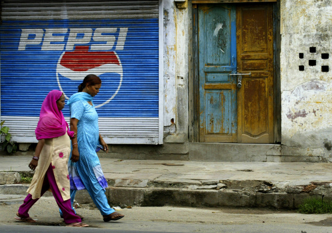 Women walk past a Pepsi advertisement in New Delhi.   Bloomberg