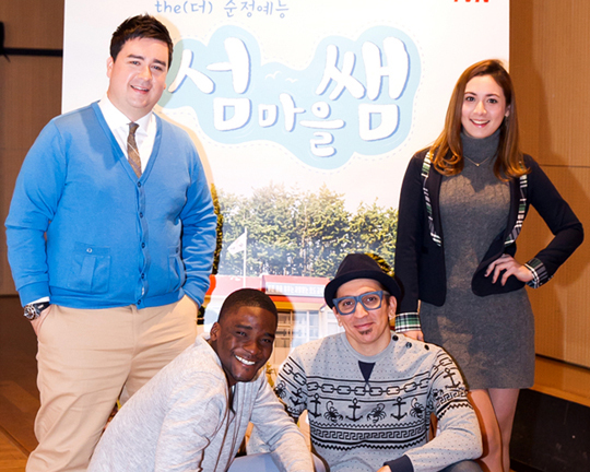 Left to right: Sam Hammington, Sam Ochiri, Brad Moore and Abigail Alderete pose in front of the poster for their new reality program “Island Village Teacher.”   tvN