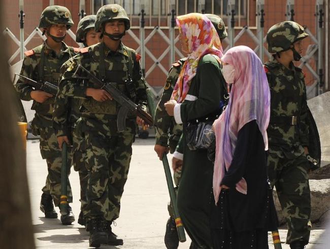 Muslim ethnic Uighur women pass a Chinese paramilatary police patrol on a street in Urumqi, capital of China’s Xinjiang region.   AFP