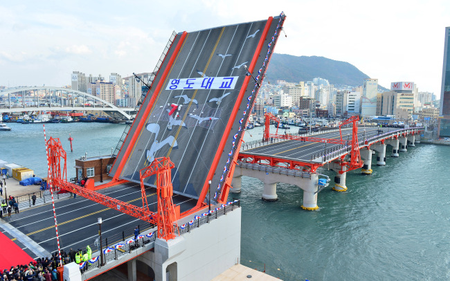 The Yeongdo Bridge in Busan is raised in a ceremony to restore the drawbridge on Wednesday. It resumed use of its moveable section 47 years after it stopped moving for safety reasons.   Chung Hee-cho/The Korea Herald