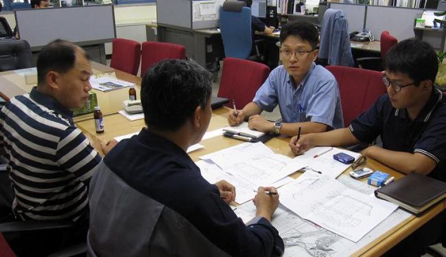 한일종합기계와 한국동서발전 임직원들이 원가절감형 공동사업의 일환으로 석탄하역용 신개념 버킷장치 개발을 위해 시제품의 성능 개선에 대한 협의를 진행하고 있다.