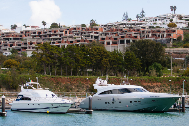 Unfinished apartment blocks stand on a hillside overlooking luxury yachts in the marina at Albufeira, Algarve region, Portugal.   Bloomberg
