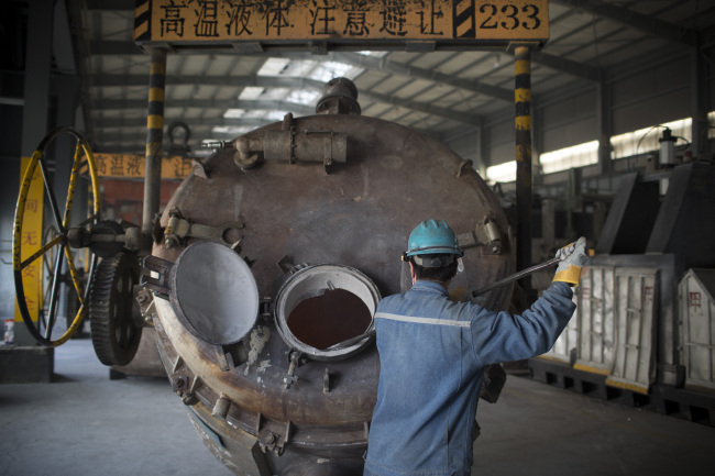 An employee cleans aluminum residue from a container at the China Hongqiao Group Ltd. aluminum smelting facility in Zouping, China.   Bloomberg