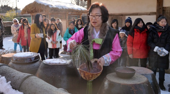Visitors to the National Folk Museum in central Seoul watch a woman sprinkle red bean porridge in the nooks and crannies of a house as part of the re-enactment of the Dongji, or winter solstice, exorcism rite on Wednesday. According to Korean traditional custom, people make the porridge and sprinkle it throughout their homes to prevent evil spirits from entering, and to wish for good luck on the winter solstice.   Lee Sang-sub/The Korea Herald