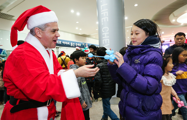 GM Korea CEO Sergio Rocha, dressed as Santa Claus, delivers a puppy-shaped balloon to a girl during a Christmas party for children at the company’s headquarters in Bupyeong, Incheon, Tuesday night.   GM Korea