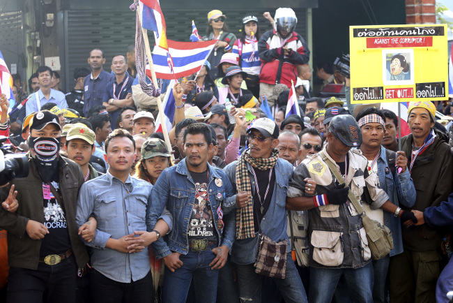 Antigovernment protesters link arms while blocking a police station near a sports stadium to prevent political parties from making a registration in the upcoming general election in Bangkok on Monday.   AP-Yonhap News