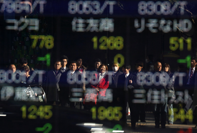 Pedestrians are reflected in a window in front of a stock board outside a securities firm in Tokyo.  Bloomberg