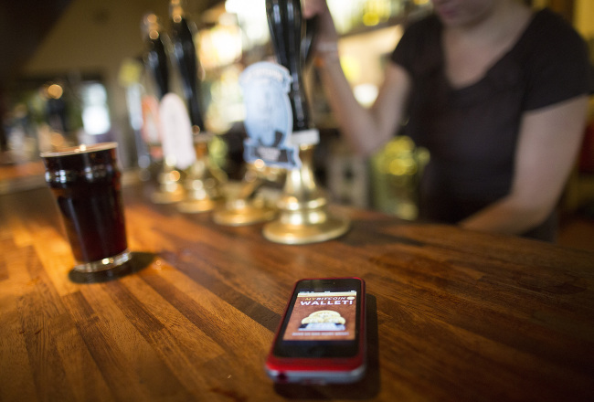 An Apple Inc. iPhone5 displays the Bitcoin Wallet smartphone app as a bar worker pours a pint of beer of the Pembury Tavern in London.   Bloomberg