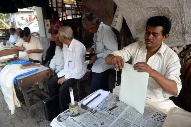 A letter writer stitches a parcel as others wait for customers at their roadside stalls, opposite the General Post Office in Mumbai.   AFP Photo