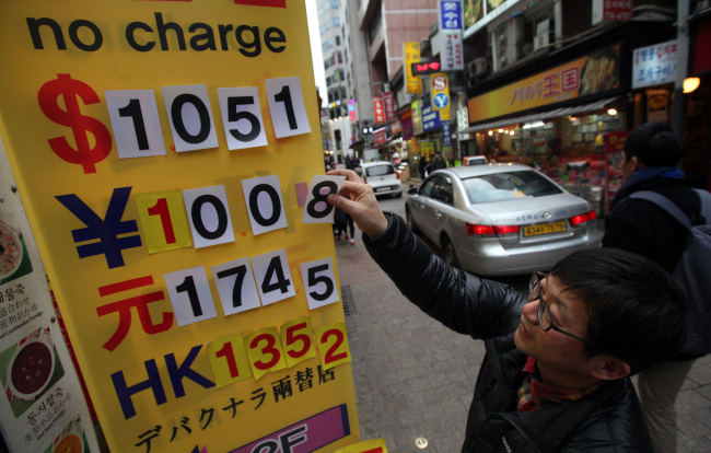 A man alters the exchange rate display in front of a currency exchange broker in Myeong-dong, Seoul, Friday.   Yonhap