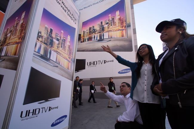 Visitors point at ads for Samsung Electronics’ curved ultra high-definition TV unveiled at the Consumer Electronics Show in Las Vegas this week.   Samsung Electronics