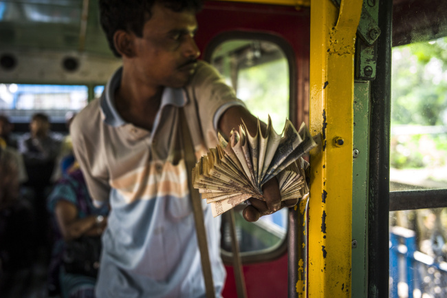 A bus conductor holds a fan of Indian rupee banknotes on a bus in Kolkata, West Bengal, India.   Bloomberg
