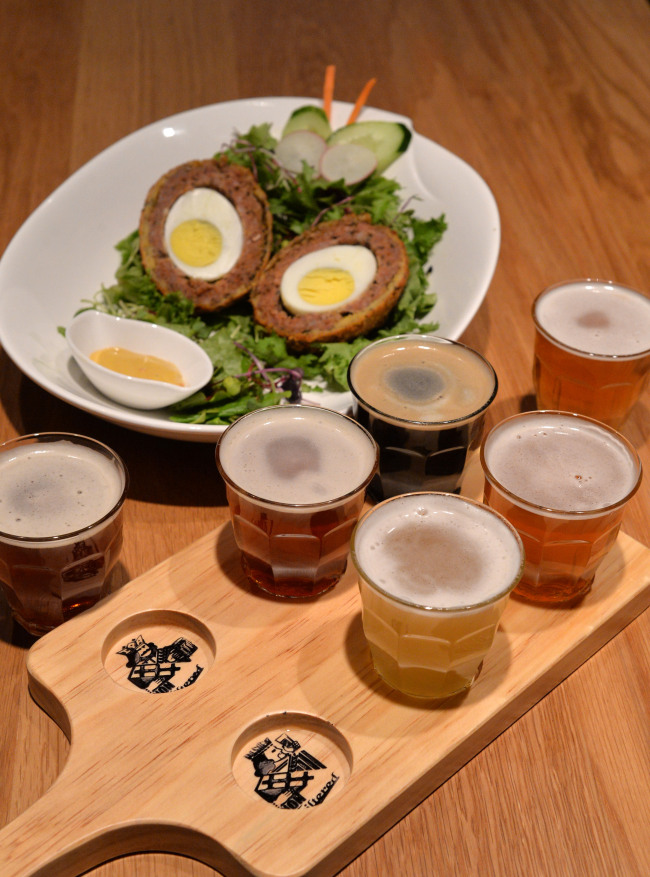 7Brau Pub’s beer sampler (front) features IPA, Mild Ale, Pilsner, Fake Lager, Kristal Weizen and Stout. The Gangnam outpost’s take on the classic Scotch egg (back) pairs well with the caramel notes of the Fake Lager.
(Lee Sang-sub/The Korea Herald)