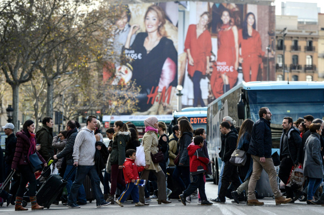 Pedestrians cross a crowded shopping street in Barcelona.   Bloomberg