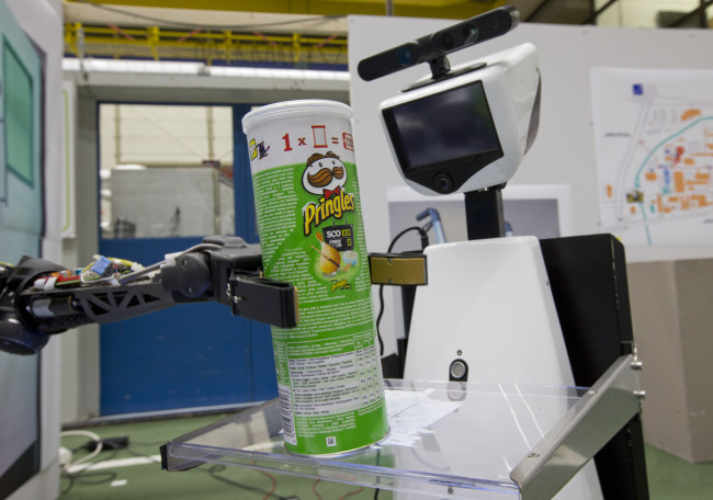 A robotic arm puts a package of Pringles on the serving tray of another robot.   AP-Yonhap News