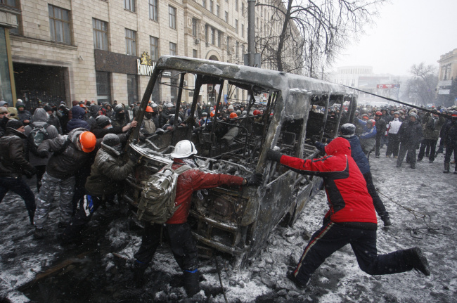 Protesters overturn a burnt-out vehicle at the site of a standoff between riot police and demonstrators in central Kiev on Tuesday.   Itar-Tass-Yonhap News