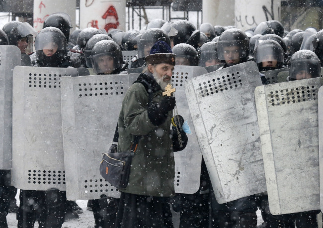 An Orthodox priest prays in front of police officers as they block a street after clashes in central Kiev on Wednesday.   AP-Yonhap News