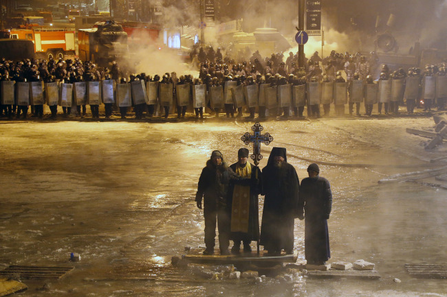 Orthodox priests pray as they stand between pro-European Union activists and police lines in central Kiev on Friday.   AP-Yonhap