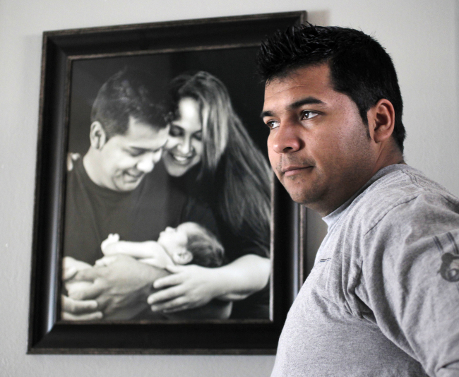 Erick Munoz stands with an undated copy of a photograph of himself (left) with wife Marlise and their son Mateo, in Haltom City, Texas.   AP-Yonhap