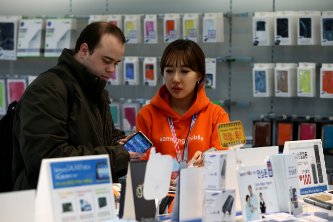 An employee helps a customer inspecting a mobile device at a Samsung Electronics Co. mobile store in Seoul.   Bloomberg