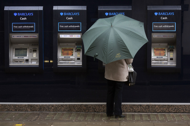 A customer shelters beneath an umbrella as she uses an automated teller machine outside a Barclays Plc bank branch in London.   Bloomberg