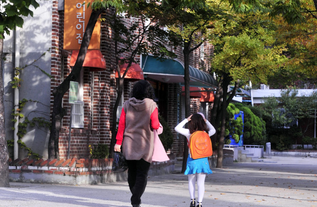 A mother walks with her child to drop her off at a school in Seoul.   Korea Herald file photo