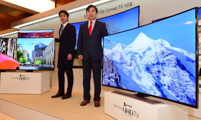 Kim Hyun-seok (right), head of Samsung Electronics’ visual display unit, and Hong Myung-bo, head coach of the Korean national soccer team, pose with the world’s first curved ultrahigh-definition televisions at the company’s unveiling event in Seoul, Thursday.   Lee Sang-sub/The Korea Herald