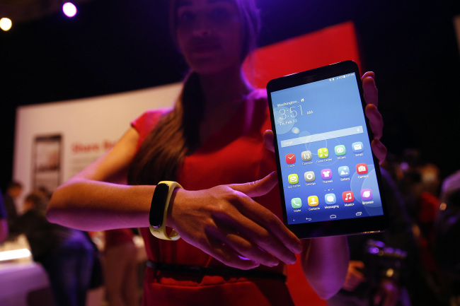 An employee displays a MediaPad X1 tablet and TalkBand wearable device during a Huawei Technologies news conference ahead of the Mobile World Congress in Barcelona, Spain, Sunday.   Bloomberg