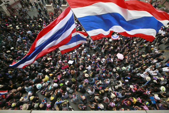 Antigovernment protesters wave national flags at the gates of the police headquarters during a memorial for the children killed in recent bomb blasts in Bangkok on Wednesday.   AP-Yonhap