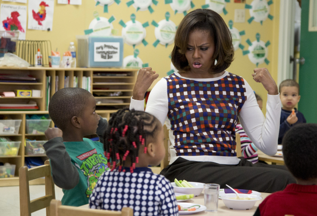 First lady Michelle Obama and a young boy show off their muscles during a visit to La Petite Academy in Bowie, Maryland, Thursday, as part of her “Let’s Move! Child Care” program.   AP-Yonhap