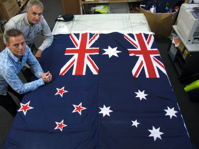 Victor Gizzi (left) and David Moginie, managers at flag manufacturer Flagmakers, pose next to flags of New Zealand (left) and Australia in their factory near Wellington on March 3.   AP-Yonhap
