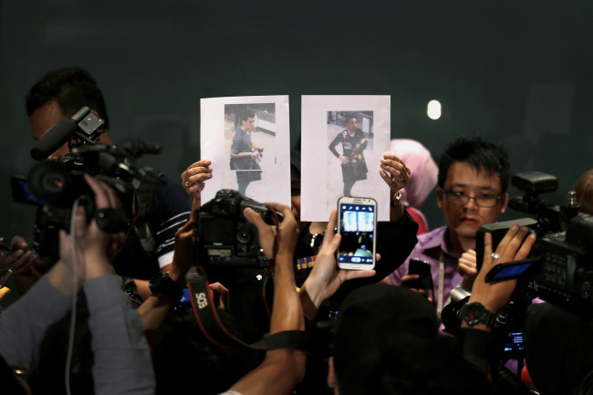 Members of the media scramble to photograph pictures of the two men who boarded the now missing Malaysia Airlines flight MH370 with stolen passports, held up by a Malaysian policewoman during a press conference in Sepang, Malaysia, Tuesday.   AP-Yonhap