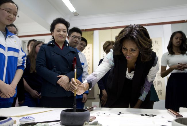 U.S. first lady Michelle Obama tries to write Chinese characters with a brush as Peng Liyuan (second from left), wife of Chinese President Xi Jinping, looks on as they visit a Chinese traditional calligraphy class at the Beijing Normal School, a school that prepares students to attend university abroad, in Beijing on Friday.   EPA-Yonhap