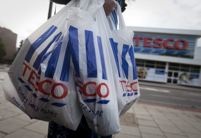 A customer carries Tesco shopping bags as she leaves one of the company’s stores in London.   Bloomberg