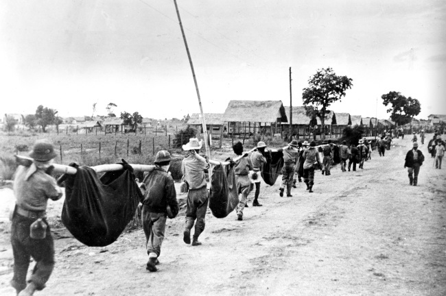 A photo released by the U.S. military in 1945, after it was captured from the Japanese, shows allied prisoners of war in the Philippines carrying their comrades in slings. In 2009, John E. Love, a Bataan Death March survivor, joined a campaign with other Bataan Death March survivors to change the caption of this photo, one of the most famous photos in AP’s library about the march.   AP-Yonhap