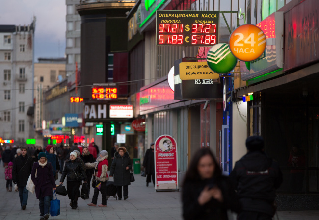 Pedestrians pass illuminated signs advertising foreign exchange rates in Moscow.    Bloomberg