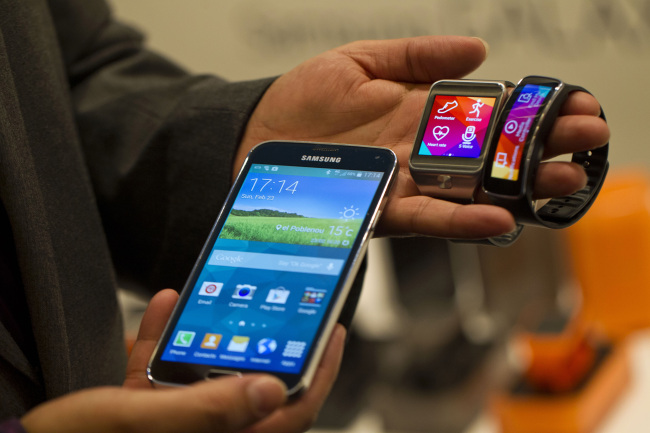 An employee displays a Galaxy S5 smartphone (left) and new Samsung Gear (center) and Gear Fit wristwatch devices at the Mobile World Congress in Barcelona in February this year.   Bloomberg