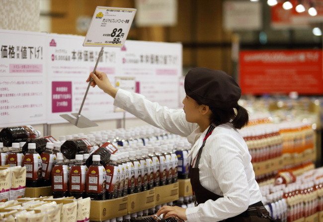 An employee places a new price sign on bottles of coffee ahead of consumption tax hike at an Aeon Co. supermarket in Chiba, Japan, Monday.   Bloomberg