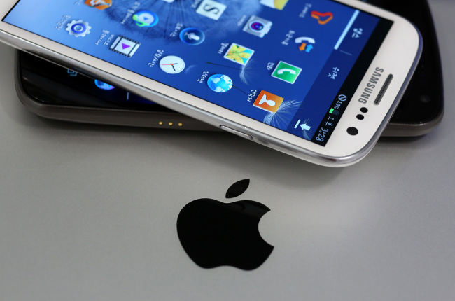 A Samsung Electronics Co. Galaxy S III smartphone (top) and a Galaxy Nexus smartphone, are arranged for a photograph next to the Apple Inc. logo in Seoul on Tuesday.   Bloomberg