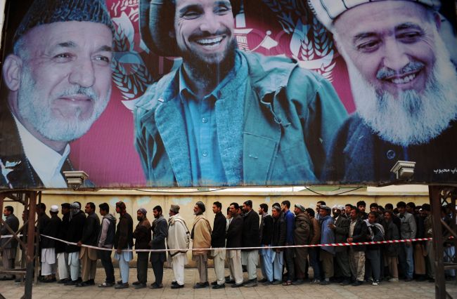 Afghan residents wishing to vote line up underneath a billboard showing images of Afghan President Hamid Karzai (left) and of deceased Afghan figures Burhandin Rabani (right) and Ahmad Shah Massoud (center) outside a polling station in Mazar-i-Sharif on Saturday.   AFP-Yonhap