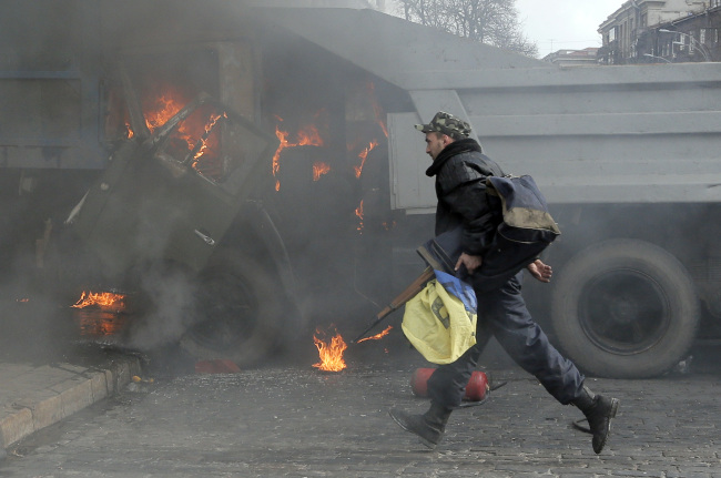 A man with a gun runs along a street during a clash at a burning barricade near the presidential office in Kiev, Ukraine.   AP-Yonhap