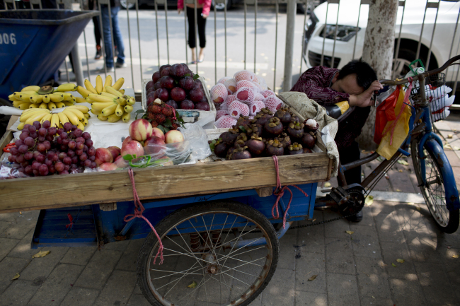 A fruit vendor leans against a bicycle as he sleeps in the Zhujiang New Town district of Guangzhou, Guangdong province, China.   Bloomberg