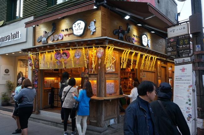 A ttakji (round comic card) gallery in Insa-dong, Seoul, hangs ice cream in cane-shaped corn puffs from its eaves.   Lee Woo-young/The Korea Herald